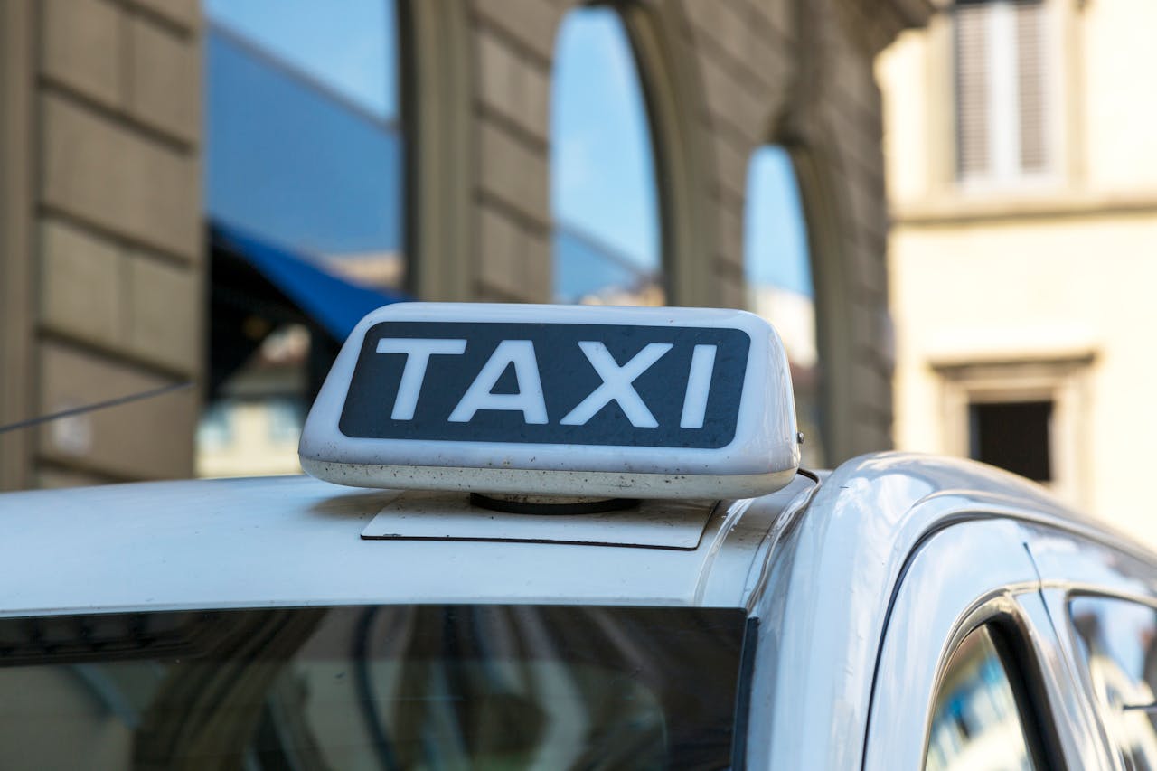 our-services-3 Close-up view of a taxi sign atop a vehicle on an urban city street with blurred architectural background.